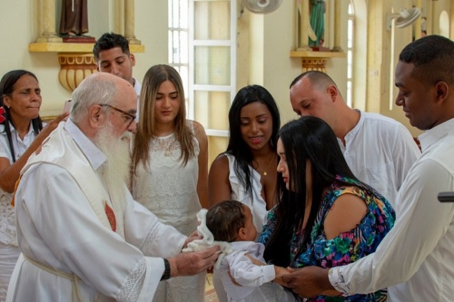 Momento cuando el sacerdote, Jorge Arcila bautiza al niño, Juan Carlos, sus padres y padrinos lo sostienen de sus manos.