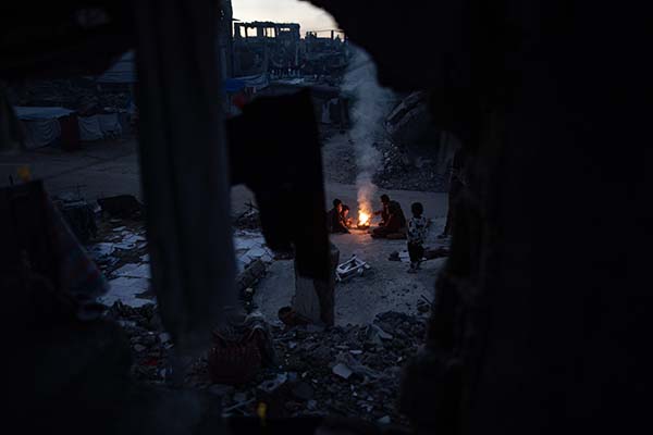 Palestinos desplazados se calientan junto a una fogata en las ruinas de su casa destrozada, este martes en Khan Yunis, Gaza. EFE/HAITHAM IMAD